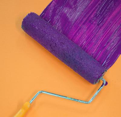 Image of paint roller covered in purple paint against a orange wall