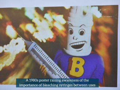 An image showing a superhero looking character with the head of a hypodermic needle, holding a giant syringe. The superhero has a 