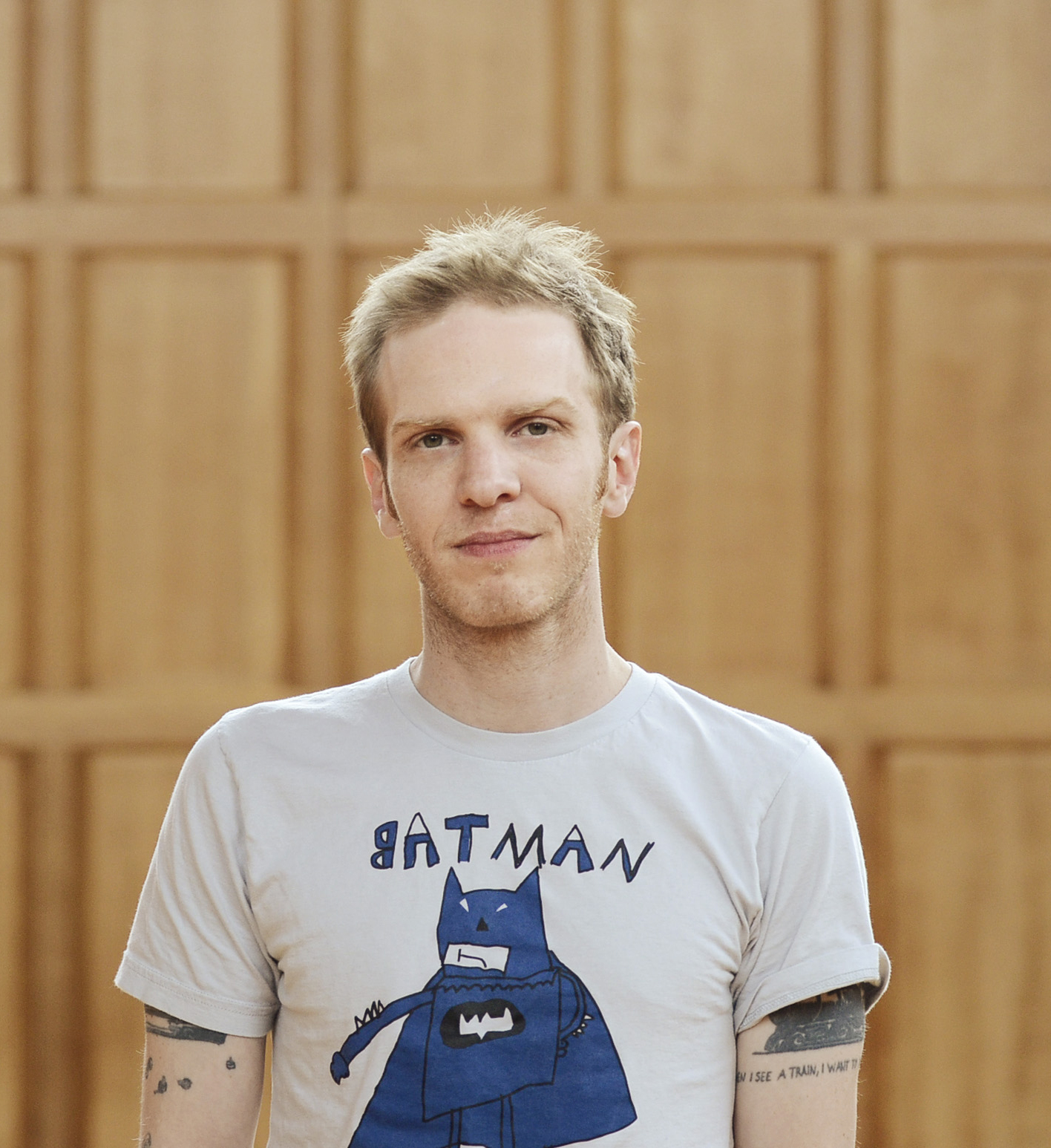 Photo of a blond, white man wearing a gray t-shirt with an illustration of Batman on it. 