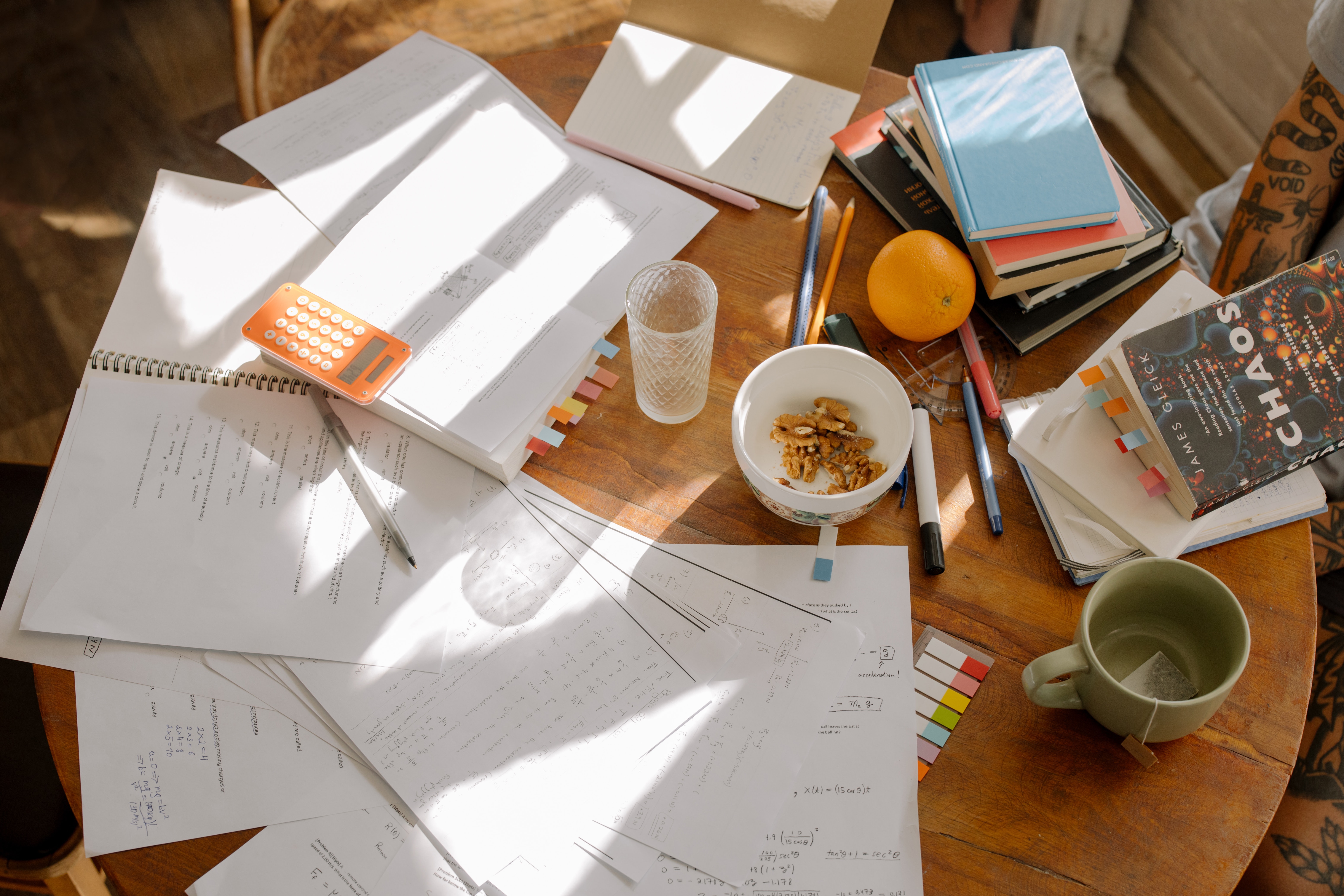 Table full of papers, books, a tea cup and an orange