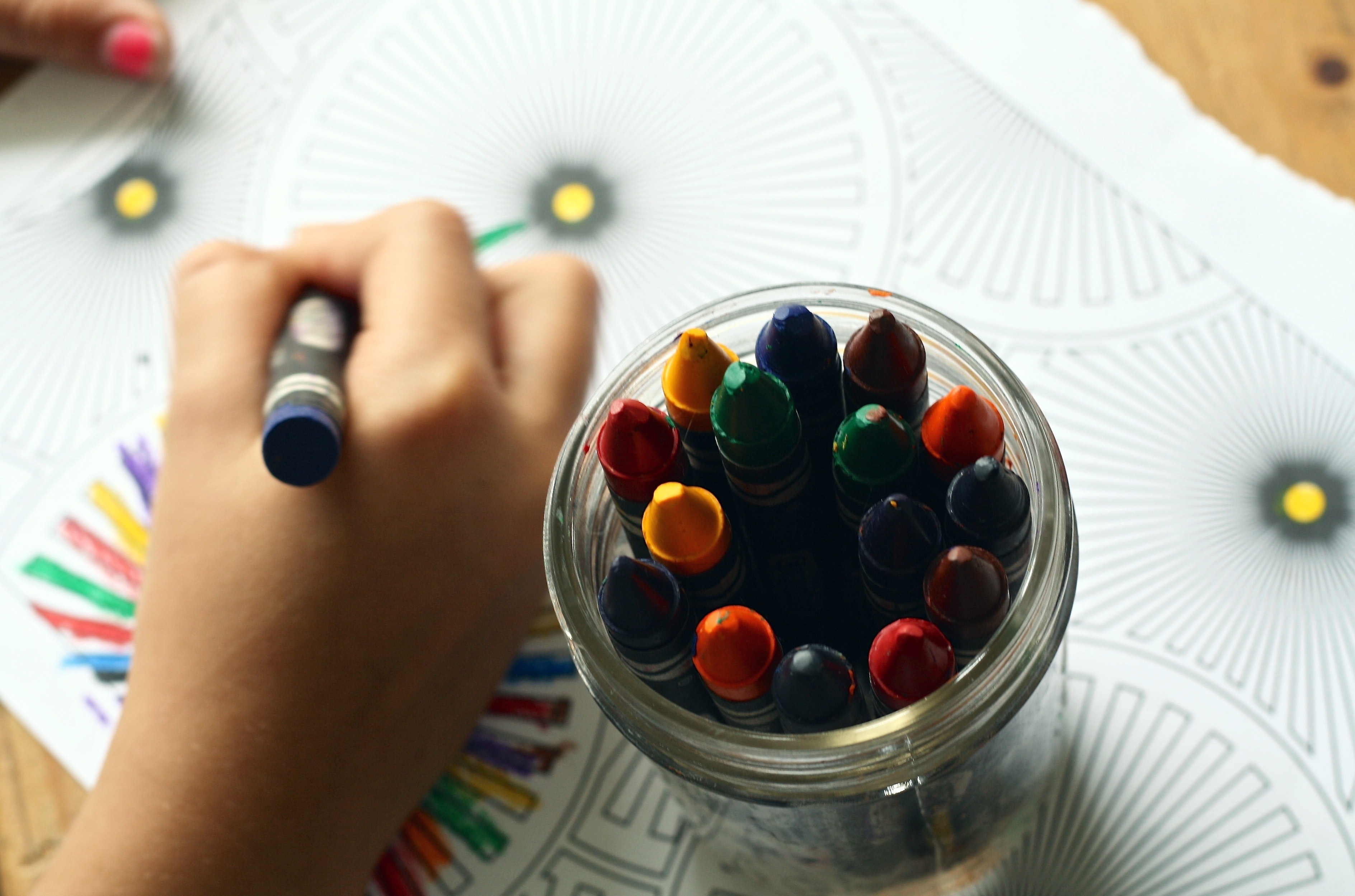 Child's hand coloring next to a jar of crayons