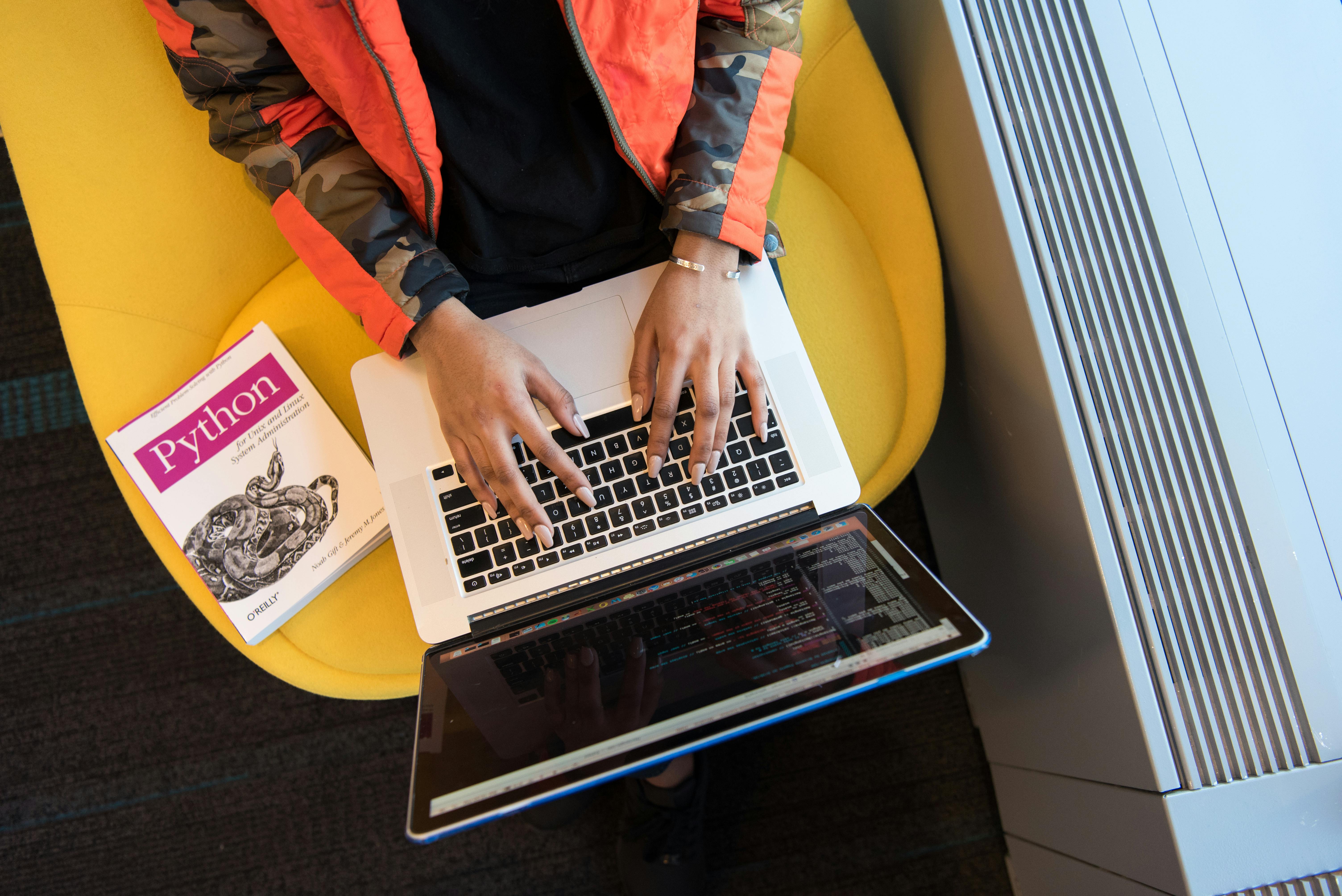 A person using a Python book at a cafe to write code on their laptop.