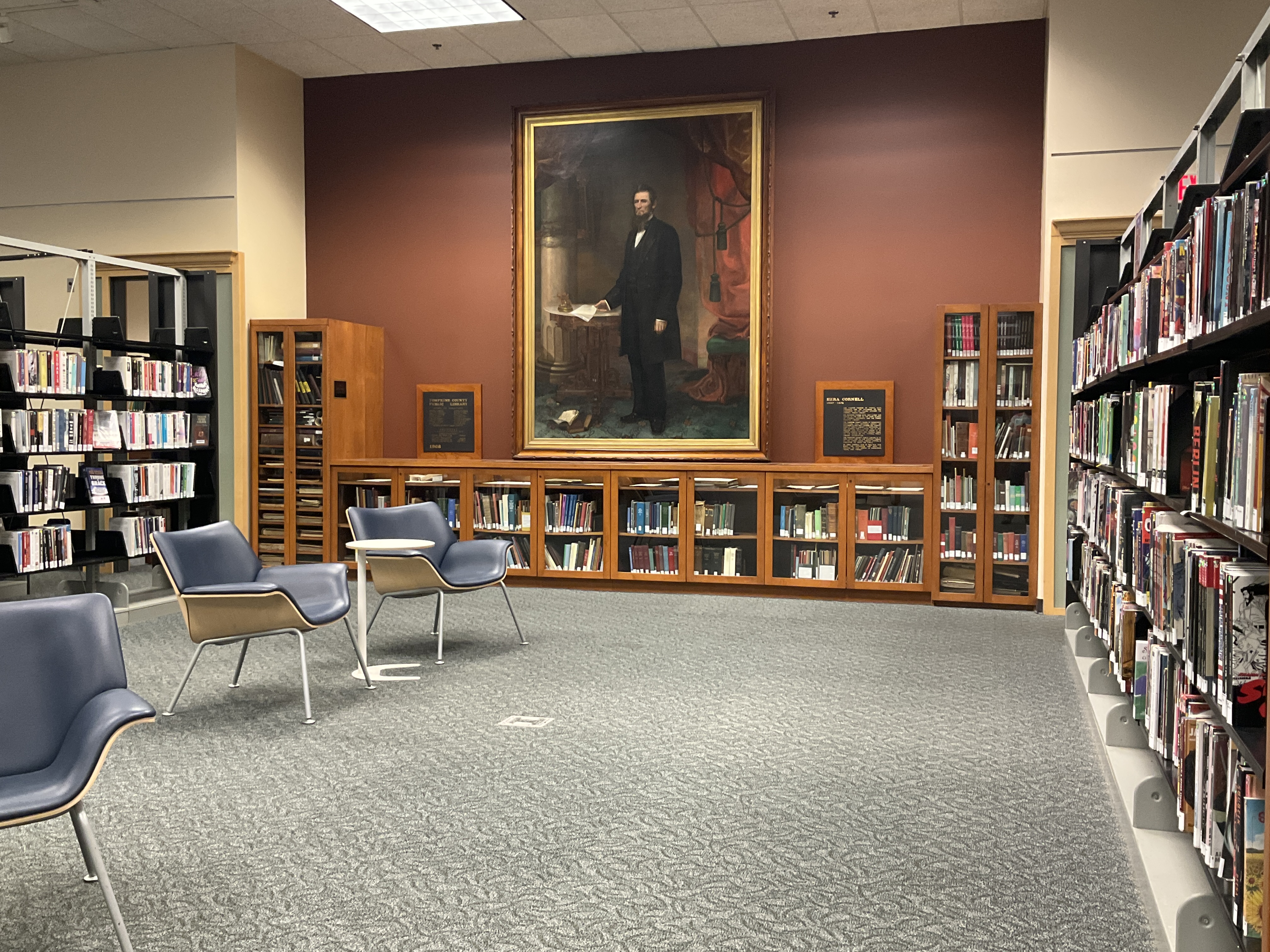 A portrait of Ezra Cornell overlooking historical books and a reading area inside TCPL