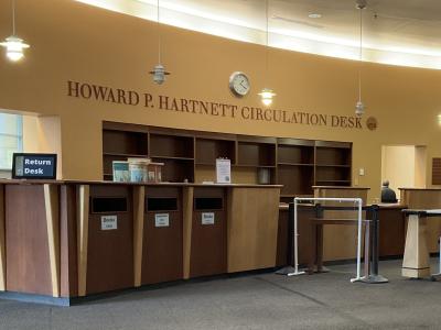An image showing the Howard P. Hartnett Circulation Desk at TCPL. It is a large wooden desk, with alternating panels of dark and light colored wood.