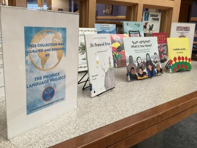 A display of books on a table outside Youth Services. It includes a sign that reads "This collection was curated and donated by The Phoenix Language Project." Books in the display include The Little Prince, What is Your Name, and Armenian Nursery Rhymes.