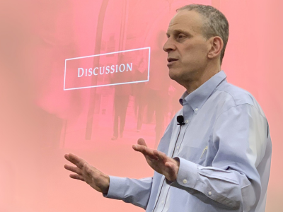 An image showing Professor Michael Dorf at TCPL, speaking to a crowd. Behind him is a red screen with the word "Discussion" prominently featured.