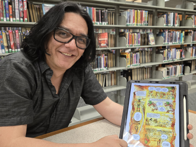A picture of Pedro X Molina holding a framed page from his forthcoming graphic novel.