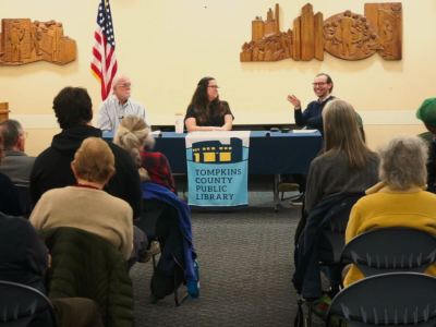 An image from inside the BorgWarner Community Room showing three people at the head of the room, sitting behind a table and speaking to a seated audience.