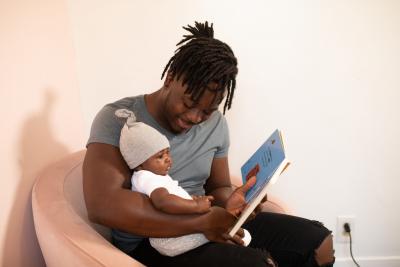 African American man reading a board book to an African-American baby.