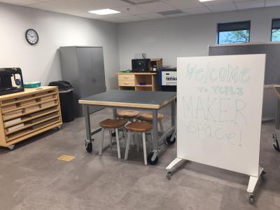 An image showing the TCPL makerspace. In the foreground is a work bench. In the background is a 50-watt lasercutting machine and 3D printers.