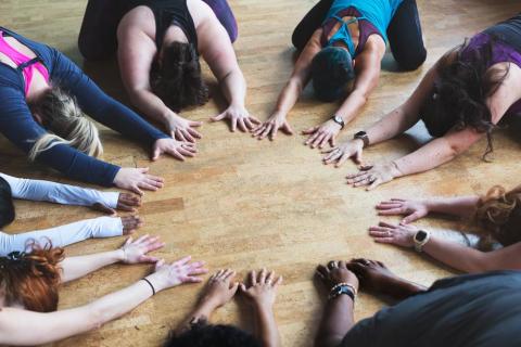 A group holds a childs pose with their hands all reaching in to form a circle