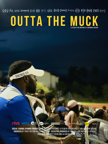 A black man wearing a white visor and blue and white shirt sitting in bleachers and looking out over the crowd towards the field.