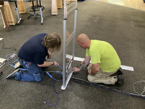 Two people work on the wiring for the RFID gates in the lobby of TCPL