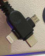 The charging adapter for a small locker. It is in the shape of a plus symbol, with lighting, micro-usb and usb-c connectors extending from the end.