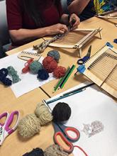 Image of patron working on loom in makerspace surrounded by yarn and other tools