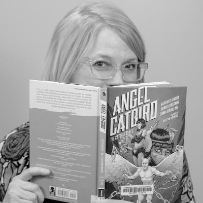 Photo of Teresa Vadakin smiling from behind a book
