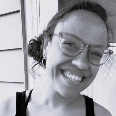 A black and white photo of Julia, a white woman with dark hair in a bun wearing glasses, smiling.